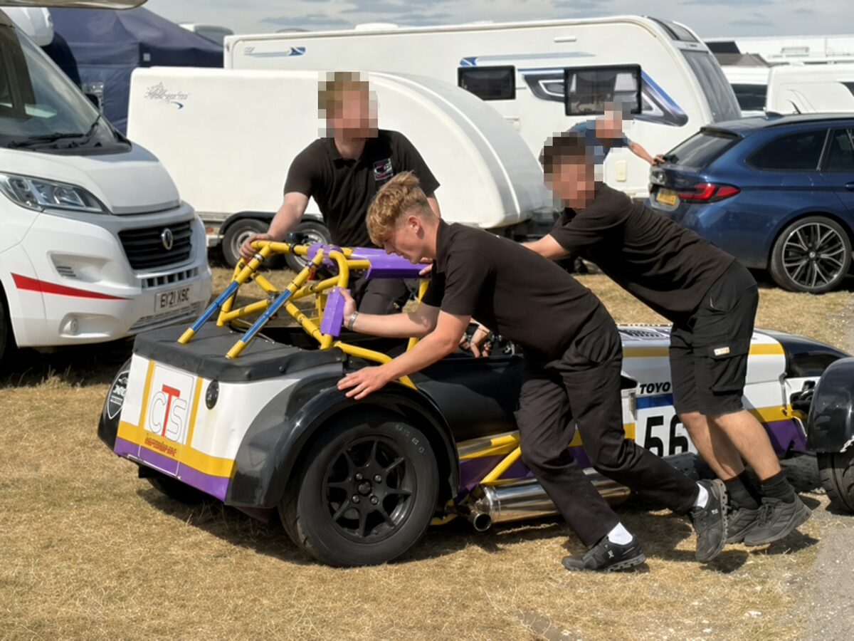 Joshua Worrall pushing a CTS Motorsport Caterham race car in the paddock